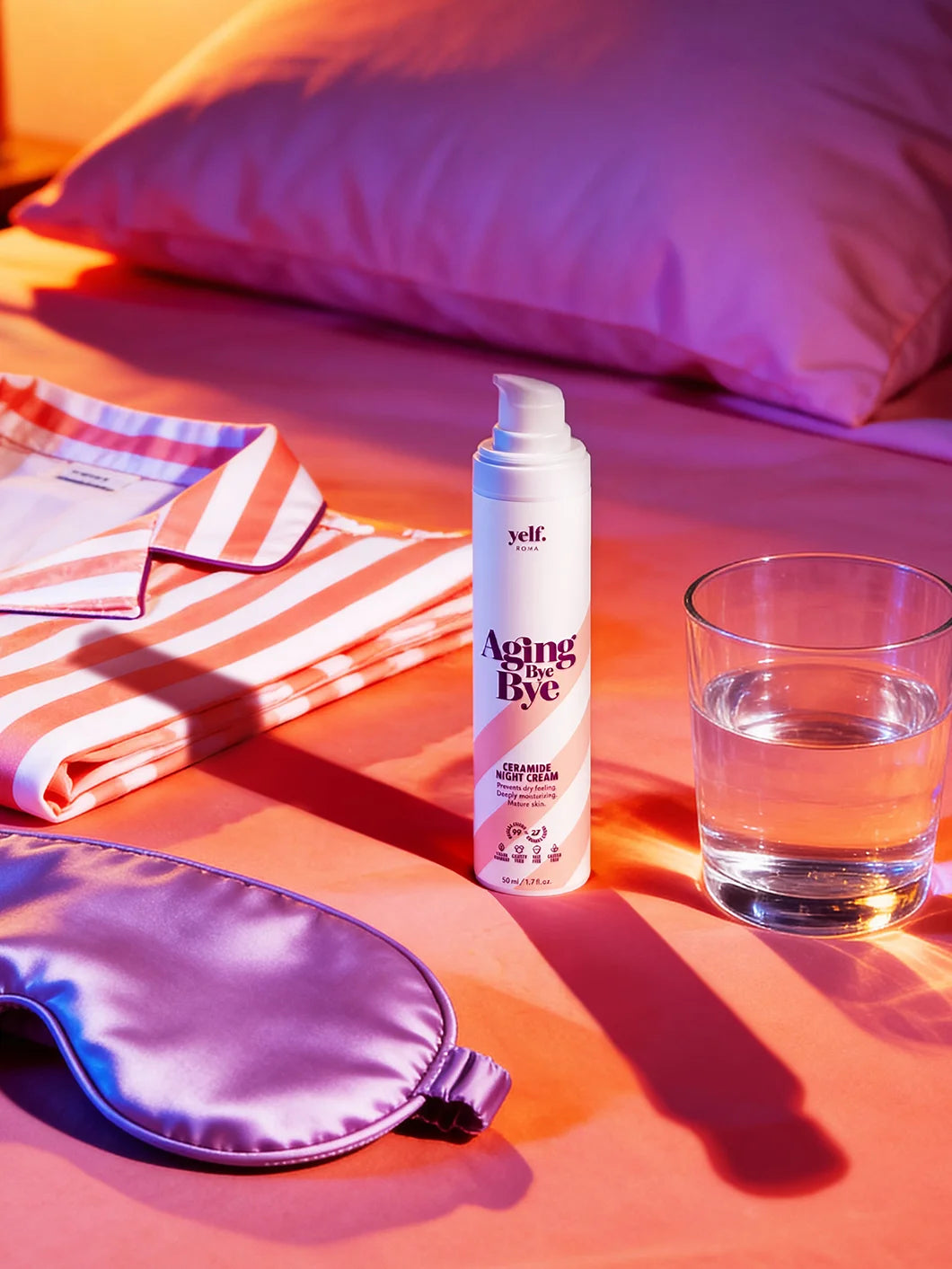 Yelf Aging Bye Bye Ceramide Night Cream standing on a neatly arranged bed with coral bedding, striped pyjama, silk sleep mask and glass of water in a bold, high-contrast night routine setting.