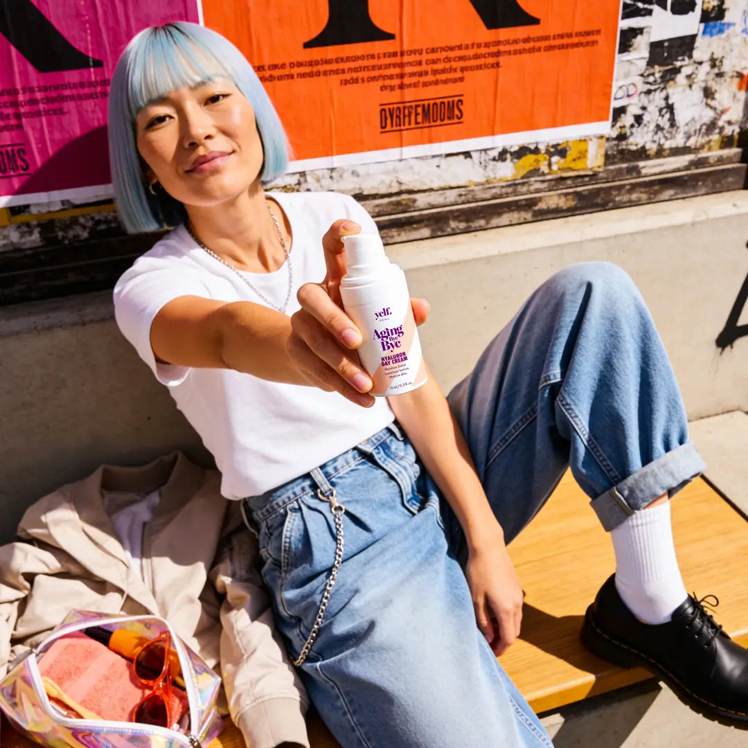 Model holding Yelf Aging Bye Bye Hyaluron Day Cream while relaxing on an urban bench in bright sunlight with colorful street posters and modern city lifestyle aesthetic.