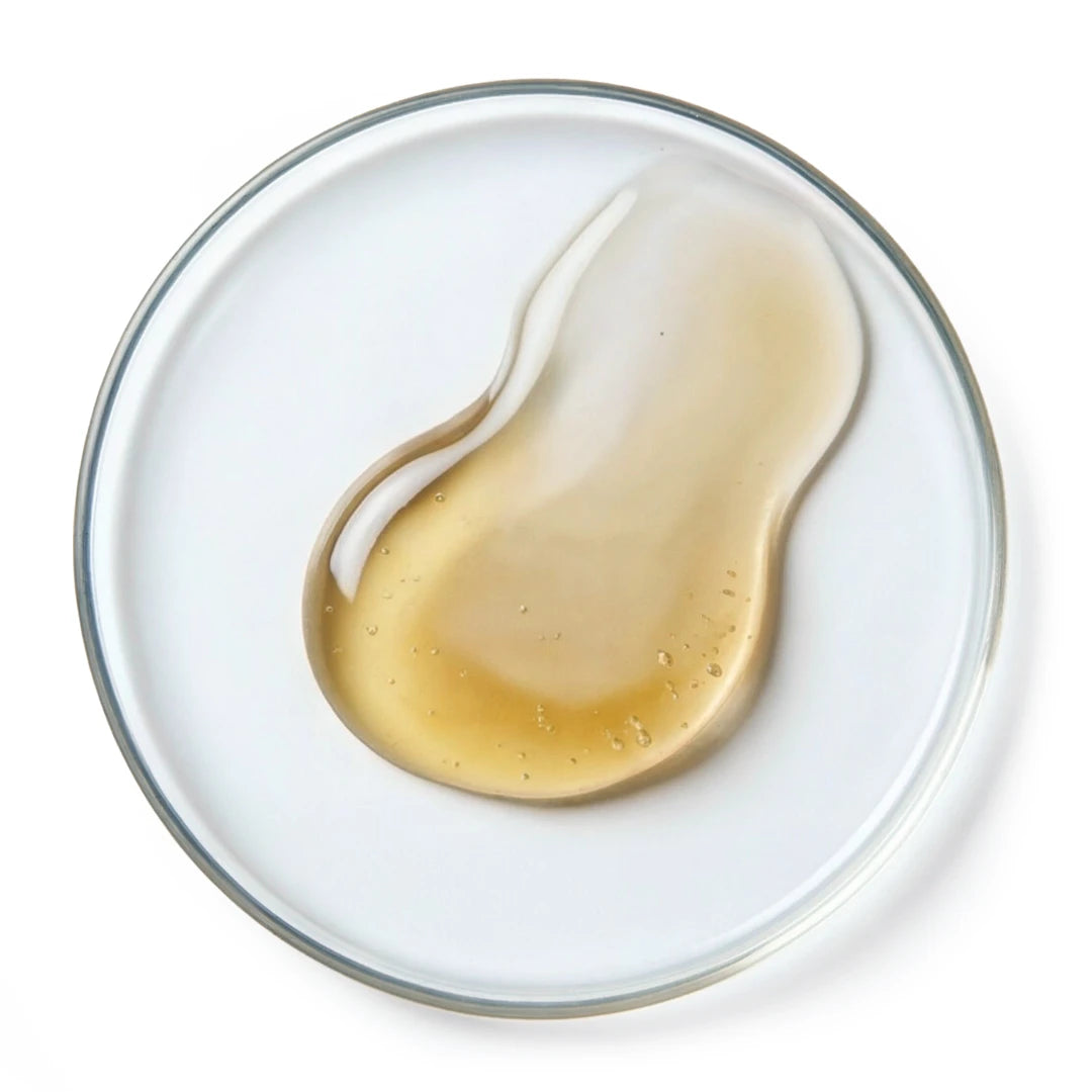 Top view of a smooth, light golden oil texture with a glossy, fluid surface on a bright white background, representing nourishing argan oil in skincare
