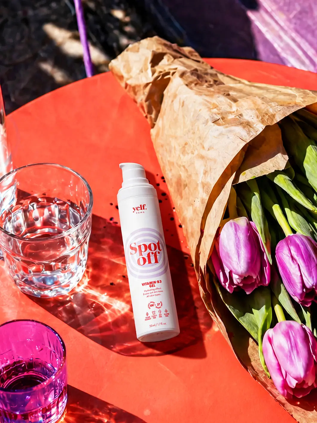Yelf Spot Off Vitamin-B3 Gel on a coral bistro table with purple tulips and water glasses in bright sunlight