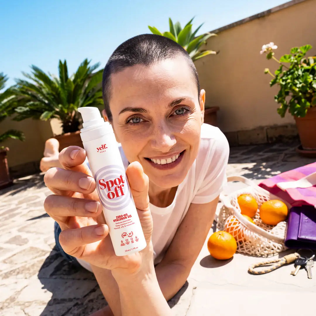 Smiling woman on a sunny terrace holding Yelf Spot Off Zero-Oil Hyaluron Gel surrounded by summer essentials and citrus fruits.